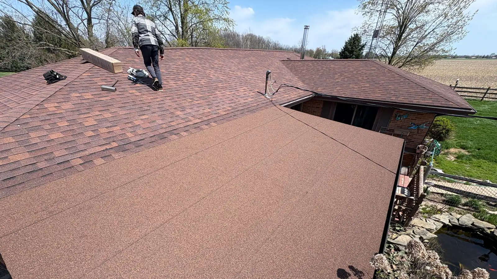 A Joe’s Roofing crew member walking a red-brown shingle roof on a ranch house.